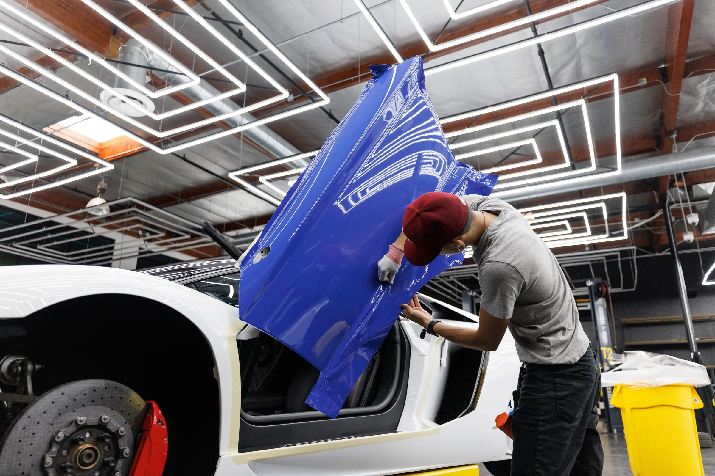 Auto mechanic applying blue vinyl wrap to a car door in a modern garage.